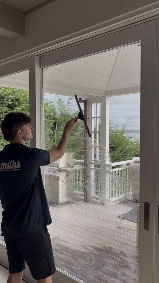Technician cleaning an interior window with a squeegee overlooking the Waitemata Harbour